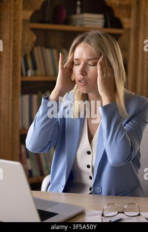 Woman touch temples with hands, feels unhealthy at workplace Stock Photo