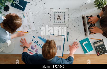 Diverse business professionals collaborate around a stylish workspace, analyzing charts and graphs with artificial intelligence technology at the cent Stock Photo