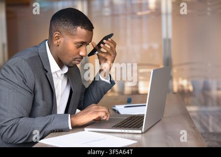 Businessman using laptop, holding smartphone, listening voice audio message Stock Photo