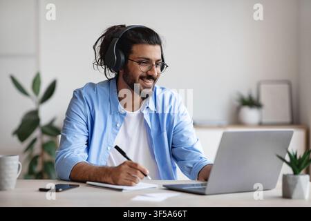 Distance Learning. Indian Guy Watching Webinar On Laptop Computer And Taking Notes Stock Photo