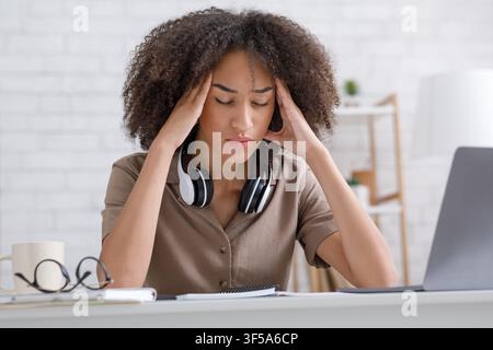 Overwork and big load. Tired business woman with closed eyes, rubs temples in interior of living room Stock Photo