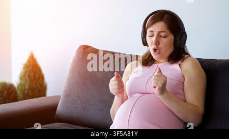 Pregnant woman listening to music and singing at home Stock Photo