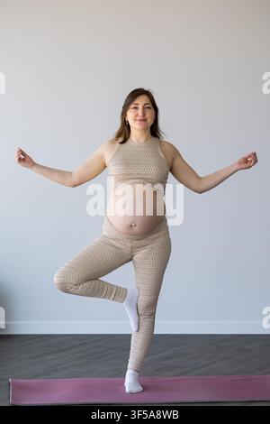 Pregnant woman practicing yoga tree pose for wellness Stock Photo