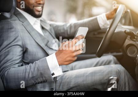 Black guy in suit using smartphone while driving Stock Photo