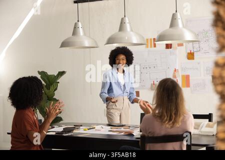 Diverse female coworkers presenting, clapping and reviewing architectural plans at studio table Stock Photo