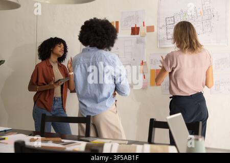 Diverse female designers working, examining pinned floor plans with tablet and swatches in studio Stock Photo