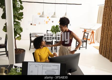 Diverse female coworkers collaborating on floor plan at studio with monitor, mustard top Stock Photo