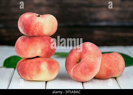 Fresh Flat Peaches, Saturn Peaches, Prunus persica var. platycarpa, on White Wooden Table with Rustic Background Stock Photo