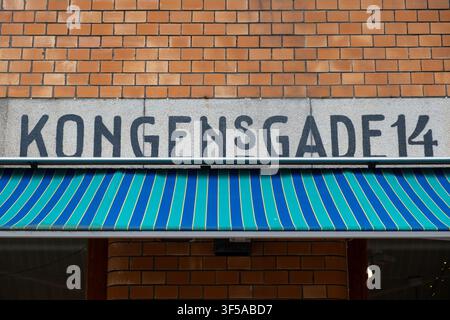 Bold painted address sign on a brick facade with a vibrant blue and green striped awning in Ålesund, Norway. Stock Photo