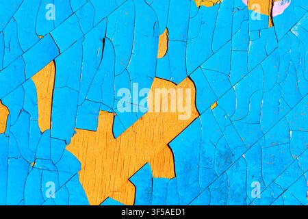 Weathered surface shows vivid peeling paint, where cracked layers of blue reveal bold orange underneath in a striking abstract pattern Stock Photo