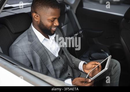 Smiling black businessman holding digital tablet in car Stock Photo