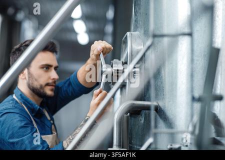 Focused Caucasian Male Technician Working With Tools In Industrial Setting, Engineering Concept Stock Photo