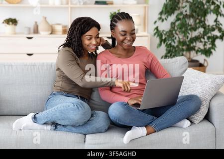 Two smiling black women using laptop at home, websurfing Stock Photo