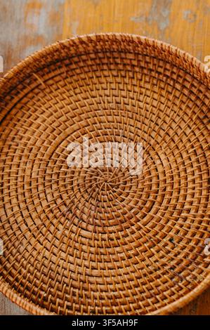 Round woven rattan basket with spiral texture resting on wooden surface, showing natural brown fibers, handmade craftsmanship Stock Photo
