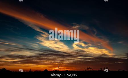 Dramatic sunset sky with sweeping orange and golden clouds above a dark rural horizon Stock Photo