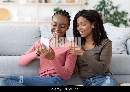Joyful black girlfriends checking photos on mobile phone Stock Photo