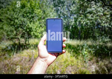Man Holding Modern Smartphone with Blank Screen Outdoors in Forest Mockup Stock Photo