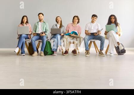 Diverse university students with laptops seated in class against gray background Stock Photo