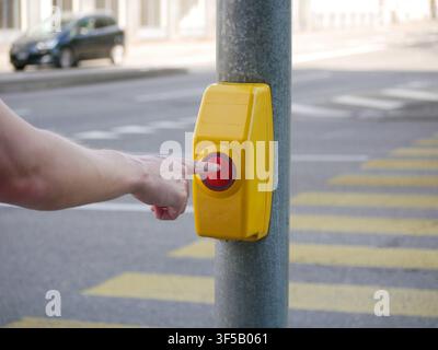 Close-up of a hand pressing a pedestrian crossing button on a traffic signal pole at a zebra crossing. Urban road safety, accessible transportation, w Stock Photo