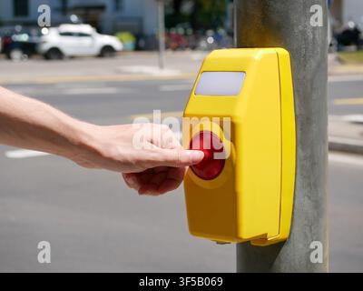 Close-up of a hand pressing a pedestrian crossing button at a signalized crosswalk in an urban environment. Concept of road safety, accessible transpo Stock Photo