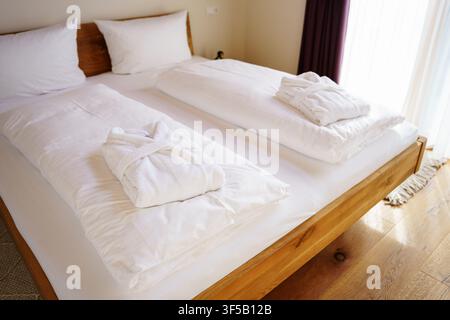 Clean white bathrobes folded on a double bed in a bright modern hotel room. Luxury hospitality service, hotel room interior, bedroom accommodation, spa wellness resort, travel trip accommodation Stock Photo
