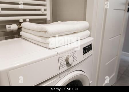 Stack of fresh clean white folded towels on top of modern white washing machine in bathroom setting. Domestic laundry room organization, textile hygiene care, minimalist home interior Stock Photo