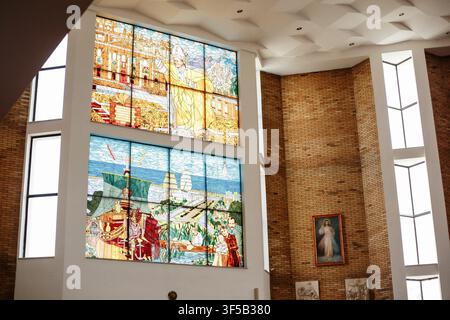 Gdansk, Poland - April 29, 2023: Interior View Of A Church With Large Stained Glass Windows Depicting A City Scene And A Religious Painting On The Wall Stock Photo