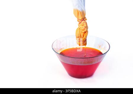 Tie-dyeing process showing knotted cotton fabric dripping orange liquid dye into a glass bowl, illustrating a creative handmade craft and DIY hobby on Stock Photo