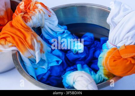 High angle view of fabric soaked in bright orange and blue dyes inside a stainless steel bowl during a creative tie-dye crafting process at home or in Stock Photo