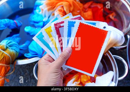 Hand holding packets of colorful powder fabric dye over metal bowls with tie-dyed clothes soaking in vibrant liquid, illustrating DIY crafting, home h Stock Photo