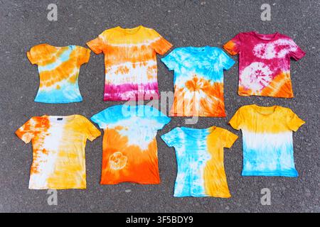 High angle view of vibrant handmade tie-dye cotton t-shirts with various spiral, swirl, and gradient patterns laid flat against a clean white backgrou Stock Photo