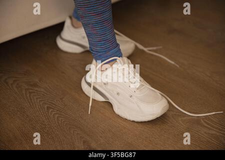 African American female showing striped leggings and white sneakers with untied laces on wood floor Stock Photo