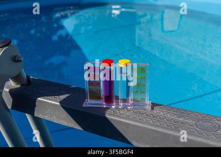 A horizontal perspective view of a chemical water quality tester kit with purple and yellow reagent liquids resting on the edge of a frame pool in bri Stock Photo