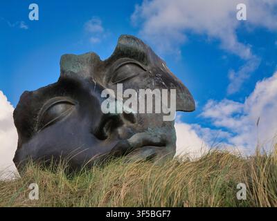 Scheveningen, Netherlands - Apr 20 2026: A weathered double face sculpture rises from dune grass beneath vivid blue skies in Scheveningen Netherlands Stock Photo