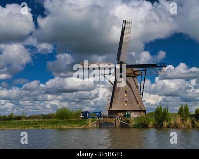 Netherlands - Apr 19 2026: A traditional windmill rises beside a canal in the Netherlands beneath dramatic spring clouds and deep blue sky Stock Photo