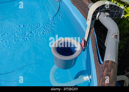 A horizontal close-up shot of a grey plastic surface skimmer basket mounted on the rim of a frame pool, skimming clean blue water under sunny weather. Stock Photo