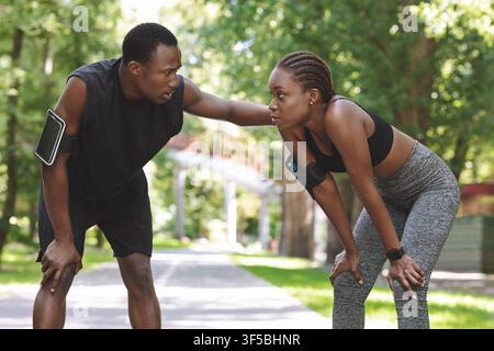 Sporty Black Couple Resting After Jogging Outdoors, Taking Breath In Park Stock Photo