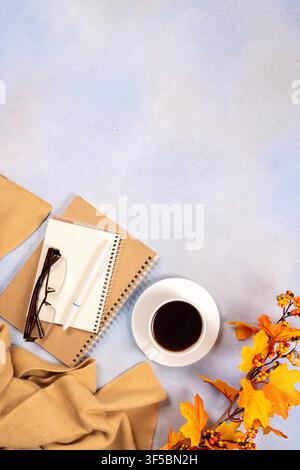 Flat lay composition showing a cozy autumn workspace with a cup of coffee, spiral notebooks, reading glasses, a pen, and a warm sweater, decorated wit Stock Photo