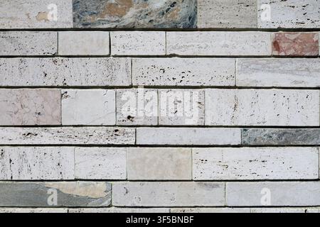 Stone coating wall made of off-white  travertine strips alternating with colored marble strips. Background and texture. Stock Photo