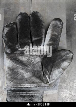 a worn leather glove resting on a surface in an indoor workshop setting, showcasing a practical and rugged mood with a top-down perspective and a mix Stock Photo