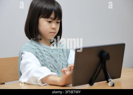 Japanese student girl using a tablet PC in dining room (8 years old) Stock Photo