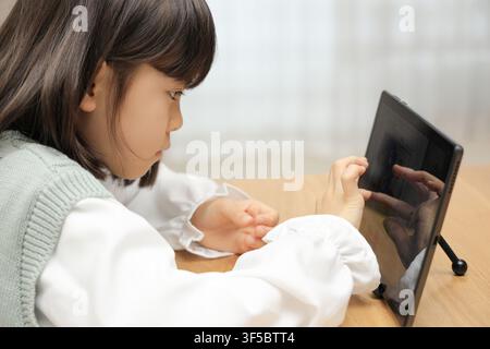 Japanese student girl using a tablet PC in dining room (8 years old) Stock Photo