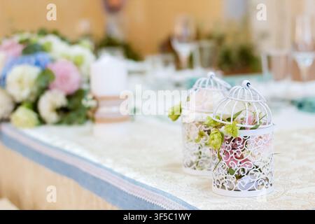 Elegant table decoration with white birdcages and pastel flowers at formal wedding reception. Romantic vintage marriage centerpiece, luxury banquet floral styling, bridal party dinner decor Stock Photo