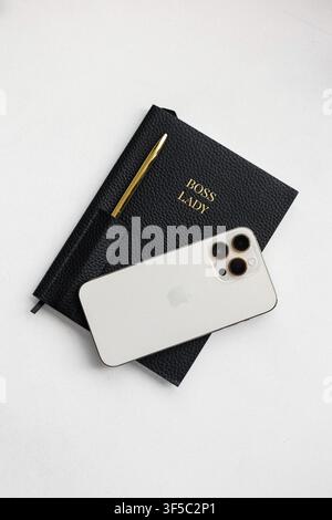 Gdansk, Poland - June 29, 2023: Minimalist black planner with a gold pen and a white smartphone on a plain grey background. Stock Photo