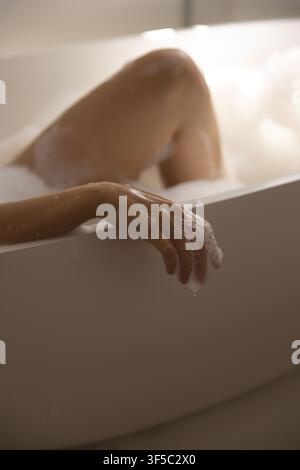 African American female reclining in bathroom in tub, arm resting on rim with soap suds Stock Photo