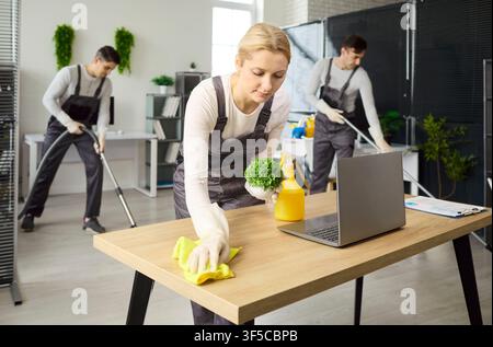 Office cleaning team with woman wiping desk, janitors mopping and vacuuming Stock Photo