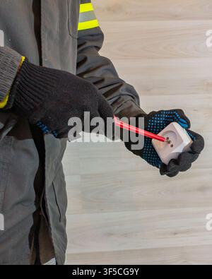 Electrician repairing electrical socket with screwdriver, male hands in protective gloves fixing wall outlet during home electrical repair and mainten Stock Photo