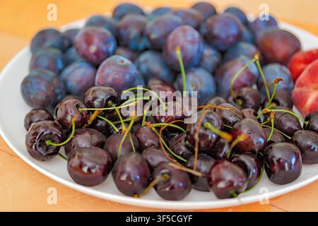 Fresh ripe dark sweet cherries and blue plums served on a white plate, close up. Stock Photo