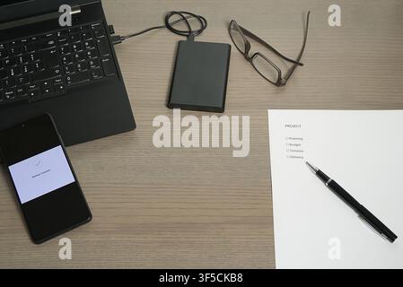 Overhead view of a desk with a "Project" task list, laptop, and smartphone confirming a successful data backup. Stock Photo