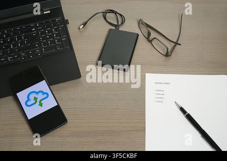 Office desk featuring a laptop, external hard drive, and a smartphone displaying a cloud synchronization icon. Stock Photo